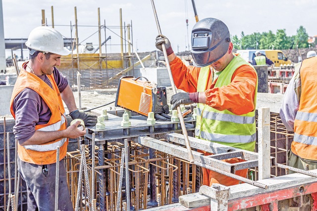 Zrenjanin, Vojvodina, Serbia - May 29, 2015: Industrial shot of construction workers who are welding metal frame, cage of armature inside of demountable wooden mold for concreting pillar base.